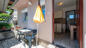 A patio with a table and chairs, an umbrella, and a view into a kitchen. - 1 bedroom beautiful apartment in Pula (Pula)