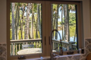Vista desde la ventana: altas palmeras y una masa de agua, con una barandilla y una silla a la vista.