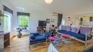 A modern living room with a sofa, a coffee table, and a TV. There is a window with a view of greenery outside. - Amazing home in Svetvincenat with WiFi (Svetvincenat)