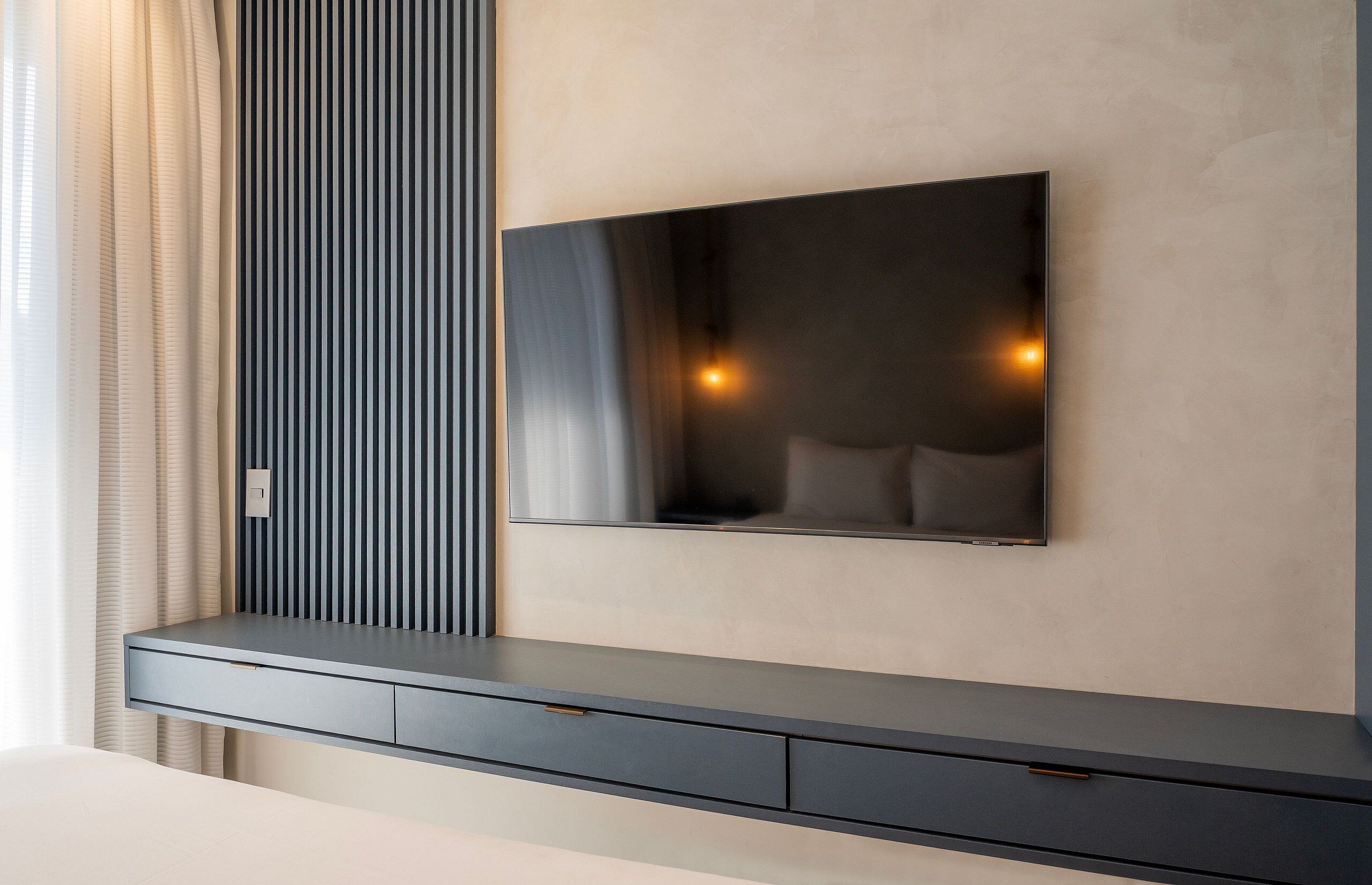 Una sala de estar moderna con un televisor de pantalla plana montado en la pared, una consola oscura y un panel a rayas verticales.