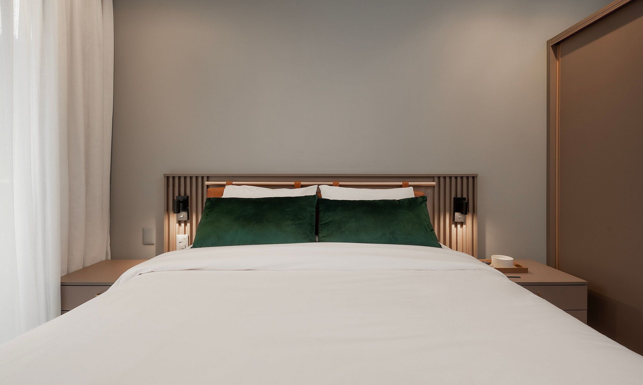 A neatly made bed with white linens, two green pillows, and a headboard with vertical wooden slats.