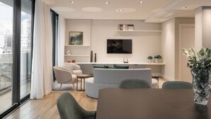 A modern living room with a sofa, chairs, a dining table, a TV, and a large window with curtains.