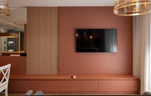 A modern living room with a large flat-screen TV mounted on the wall, a built-in bench with storage, and a pendant light fixture. - The Spot One - Luxo e acesso direto ao Balneário Shopping (Balneário Camboriú)