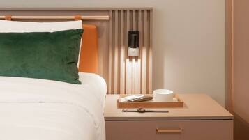 Une chambre d’hôtel bien rangée, avec un lit, une table de chevet et un luminaire fixé au mur.