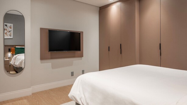A bedroom with a bed, a TV mounted on the wall, a wardrobe, and a mirror.
