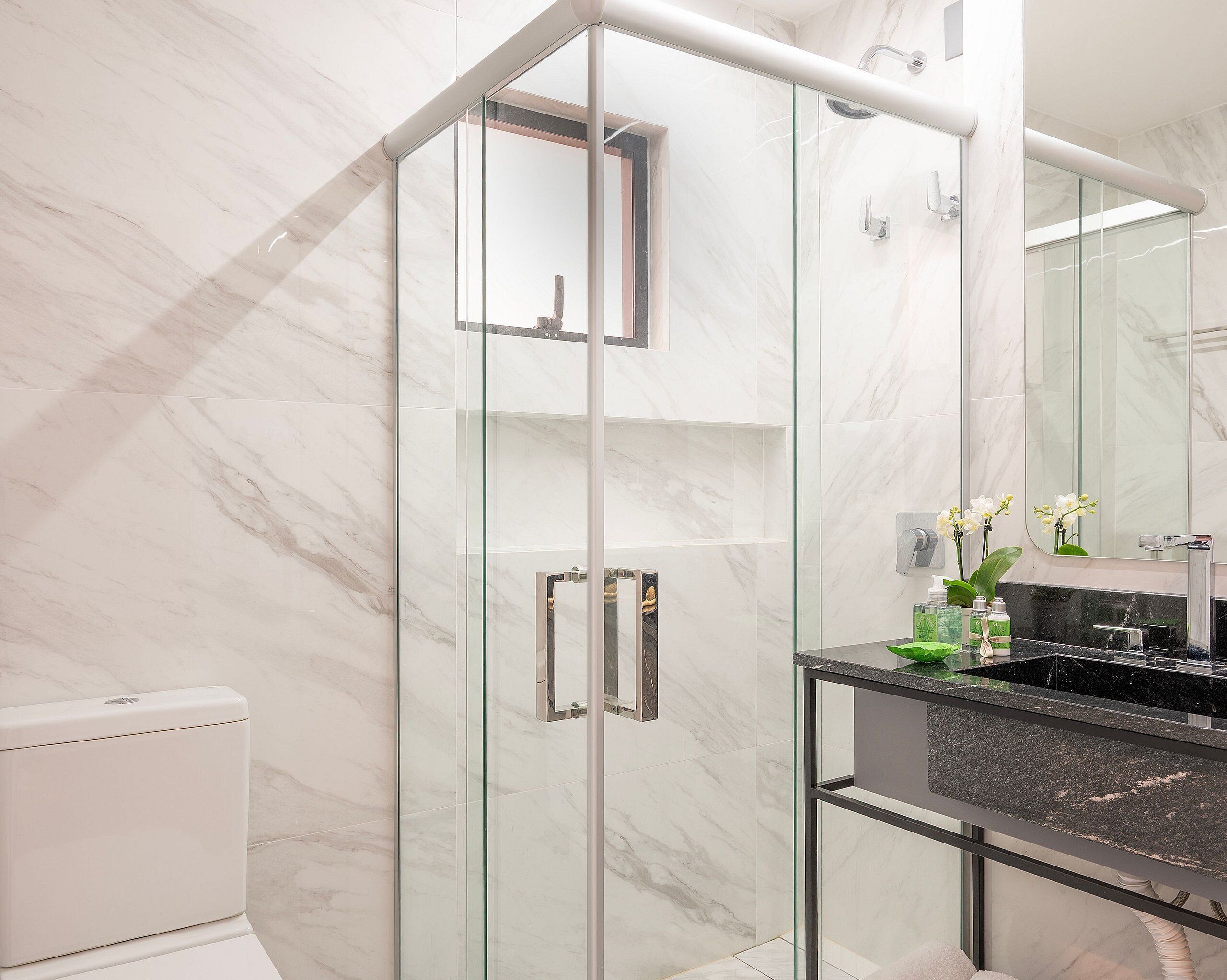Une salle de bain moderne avec une douche à parois de verre, des murs en marbre, un plan de toilette noir et un miroir.