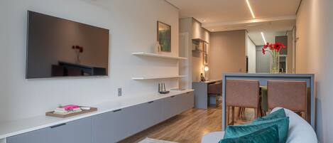Un espacio habitable moderno con un televisor de pantalla plana, un comedor con sillas y un sofá con cojines.