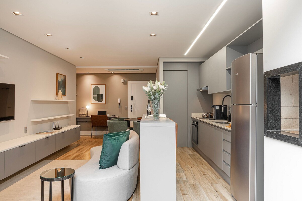 Una cocina moderna con refrigerador empotrado, una zona de comedor con mesa y sillas blancas, y una sala de estar con sofá blanco y una mesita de centro.