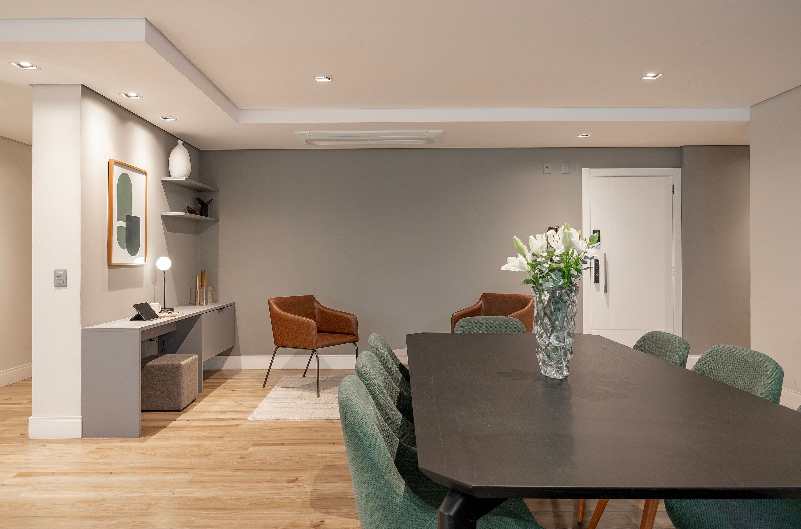 A modern dining area with a dark wooden table, green upholstered chairs, a vase with flowers, and a white console table with a lamp.