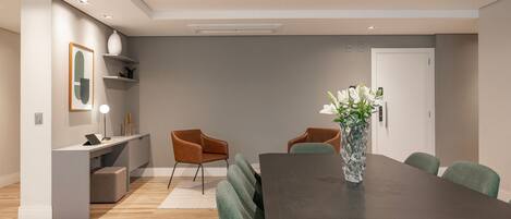 A modern dining area with a dark wooden table, green upholstered chairs, a vase with flowers, and a white console table with a lamp.