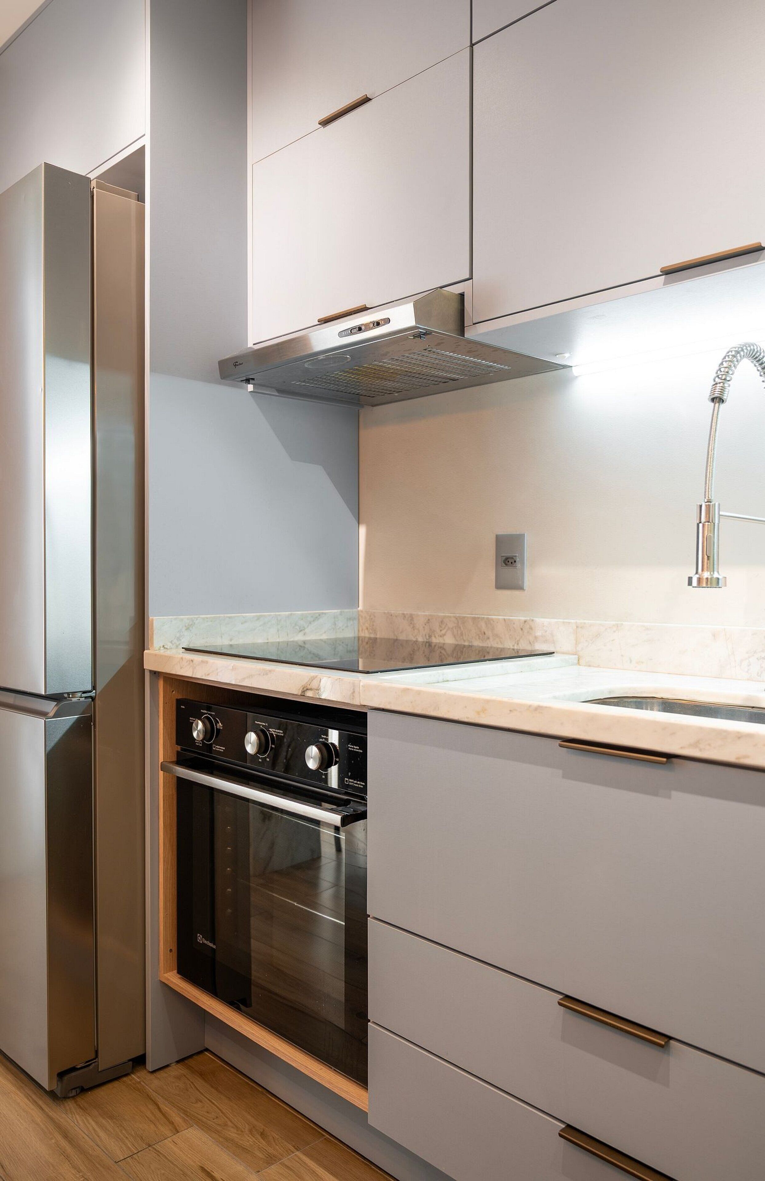 A modern kitchen with a built-in oven, stainless steel refrigerator, and a marble countertop.