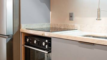 A modern kitchen with a built-in oven, stainless steel refrigerator, and a marble countertop.