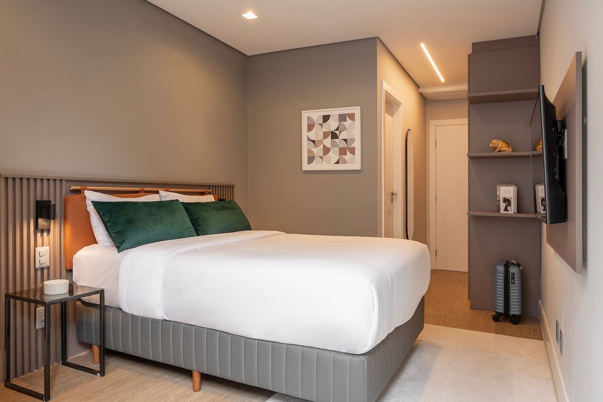 Habitació d'hotel moderna amb llit, taulell de nit i televisió penjada a la paret.