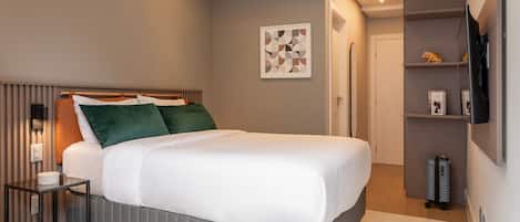 Ein modernes Hotelzimmer mit Bett, Nachttisch und einem an der Wand befestigten Fernseher.