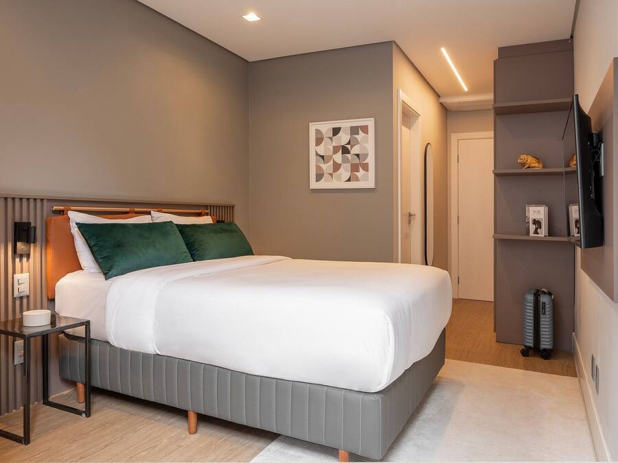 Una habitación de hotel moderna con cama, mesita de noche y televisor montado en la pared.