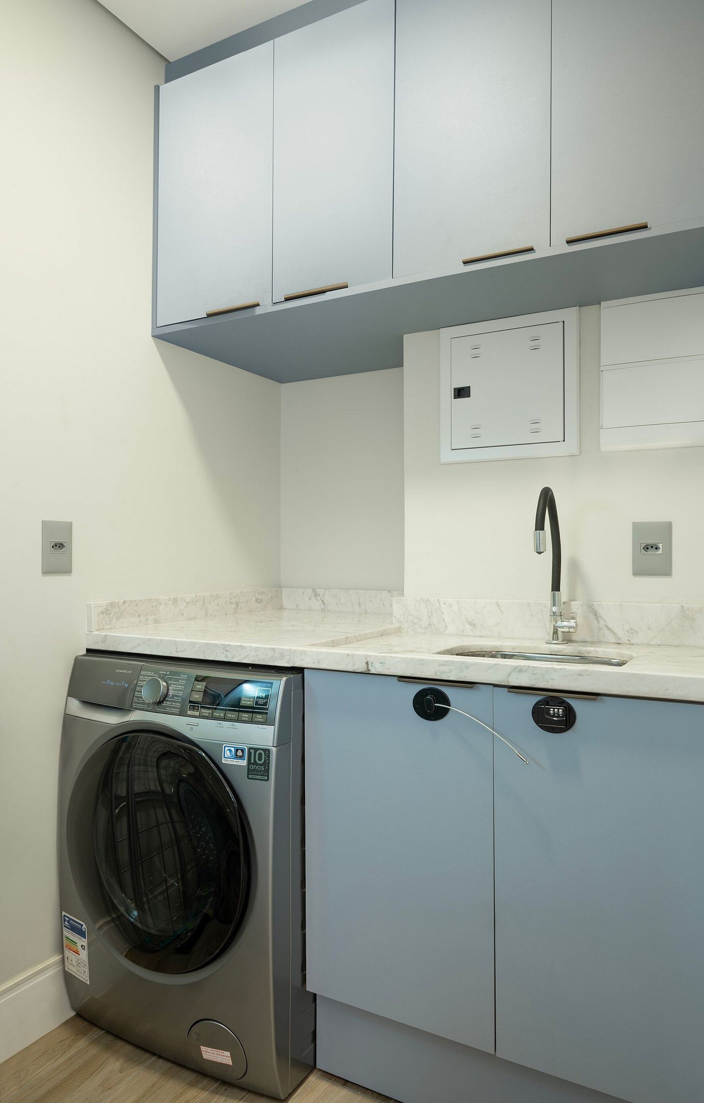 A compact laundry room with a front-loading washing machine, a sink, and cabinets above.