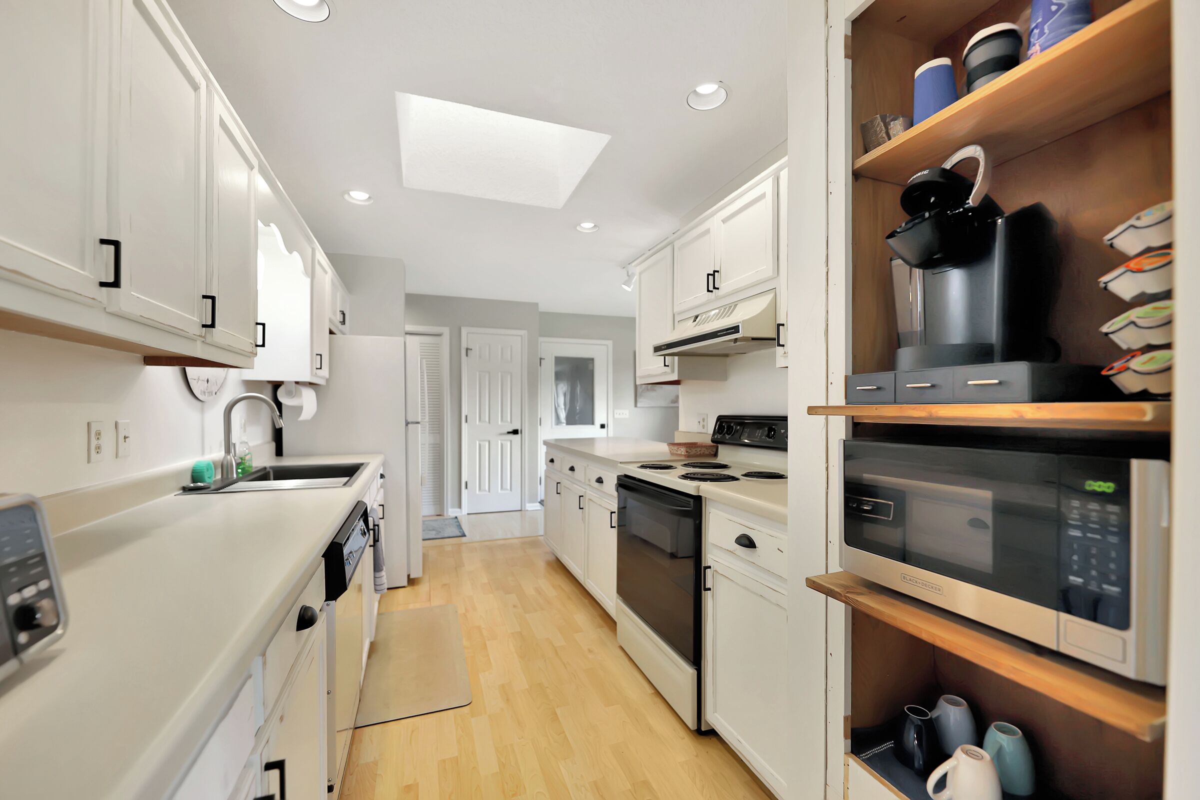 Una cocina moderna con armarios blancos, microondas, cafetera y suelo de madera.