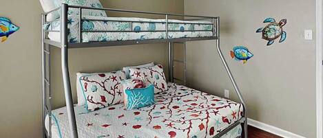 Una cama litera con una colcha estampada, una almohada y un adhesivo mural con forma de tortuga.