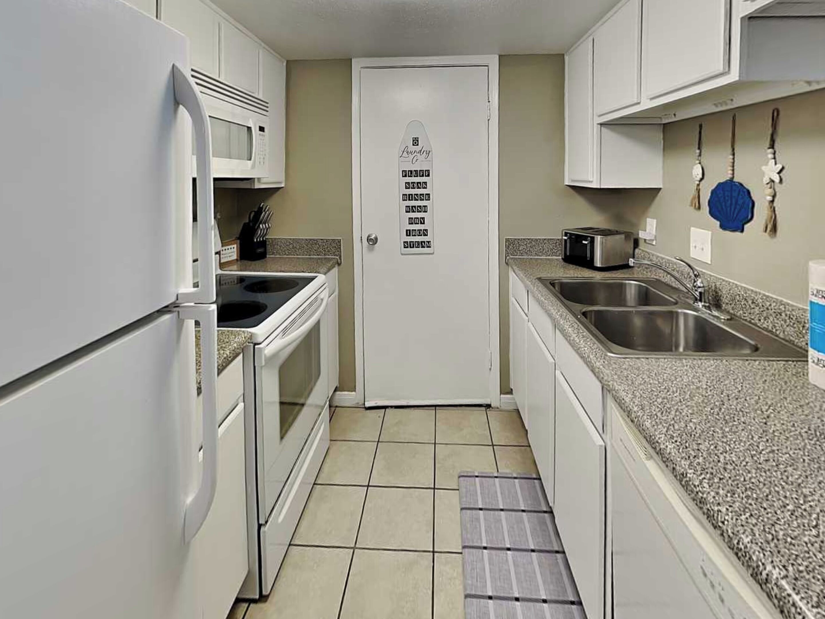A compact kitchen with a microwave, stove, sink, and a door with a list of items.