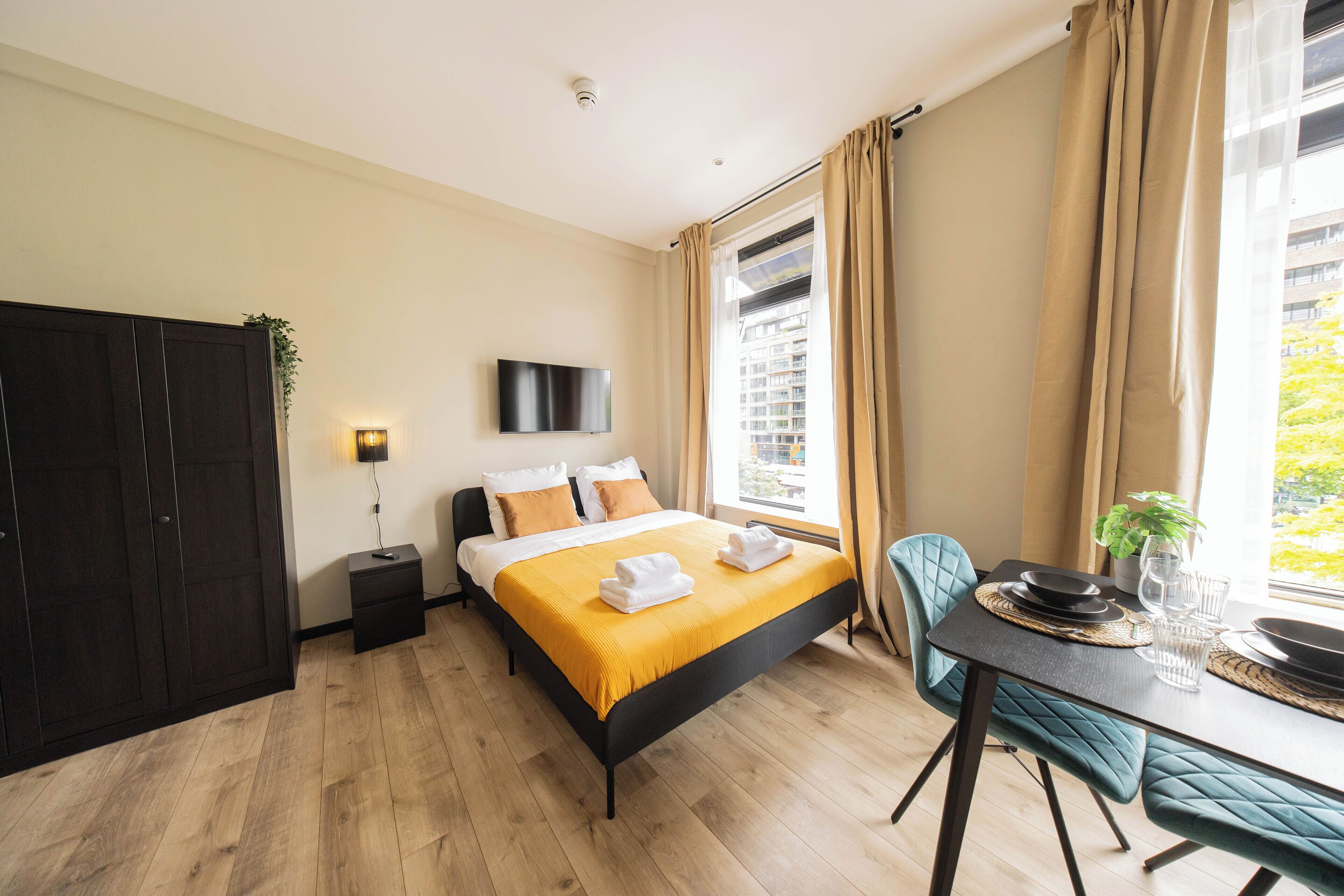 A modern hotel room with a bed, a dining table, and a TV.