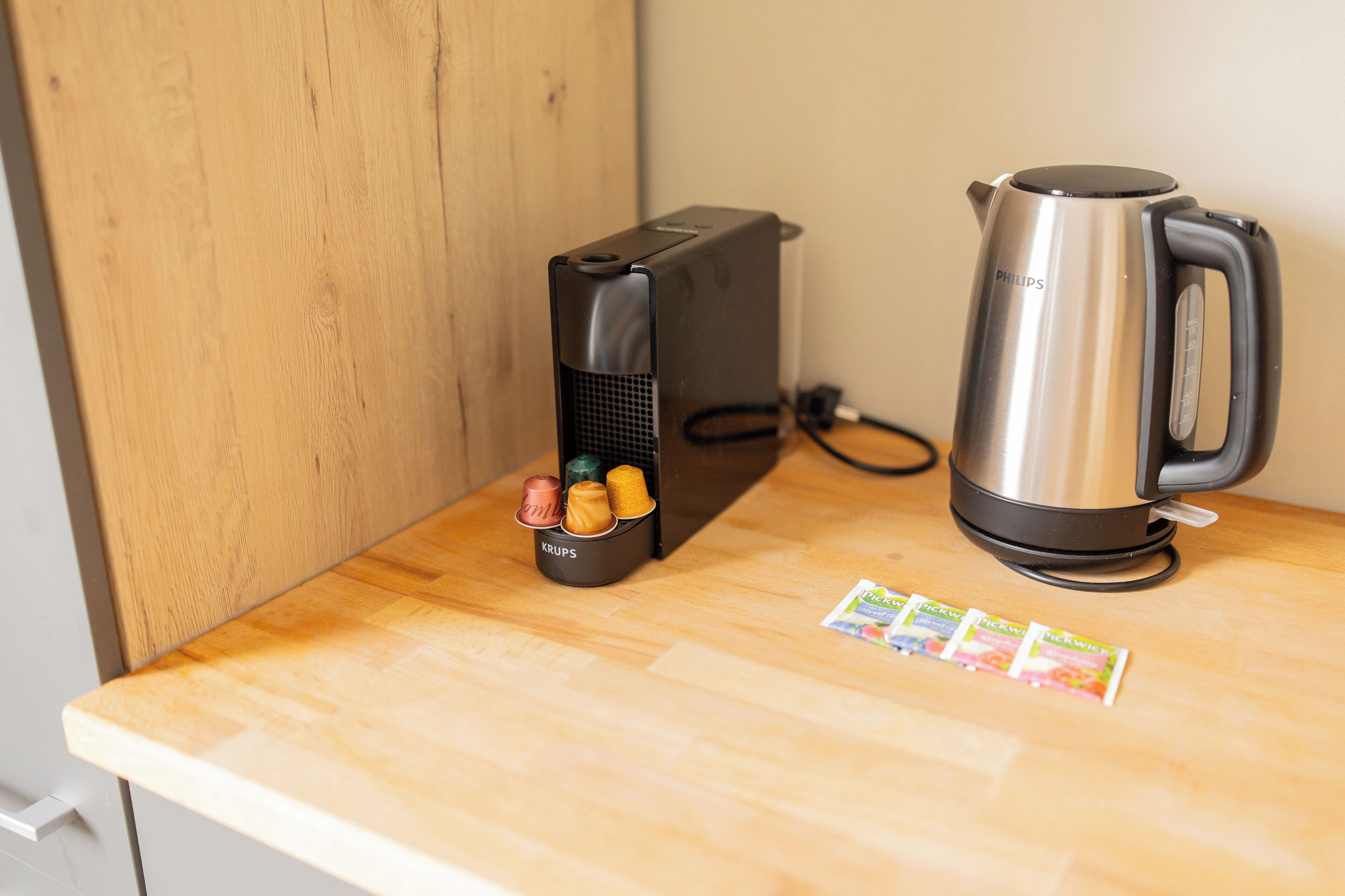 A kitchen counter with a coffee maker, a kettle, and a container holding various kitchen utensils.