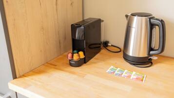A kitchen counter with a coffee maker, a kettle, and a container holding various kitchen utensils.