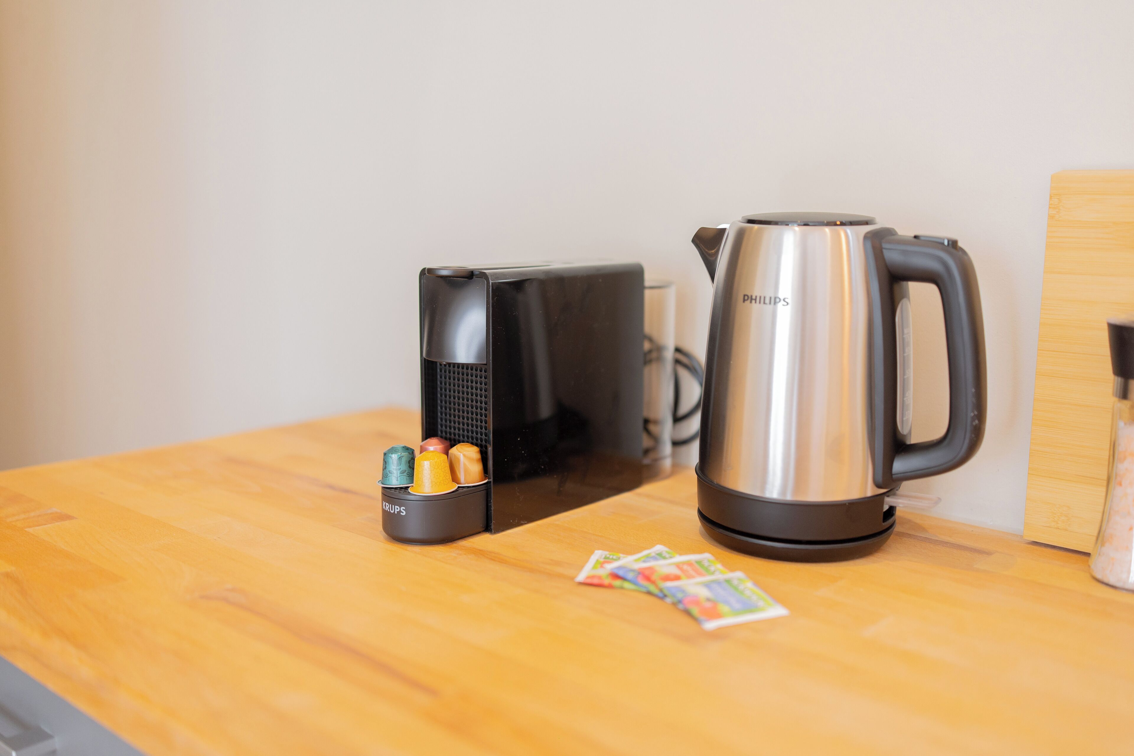 A kitchen counter with a black coffee maker, a stainless steel kettle, and a small container with colorful items.