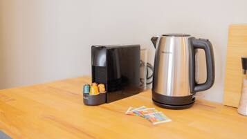 A kitchen counter with a black coffee maker, a stainless steel kettle, and a small container with colorful items.