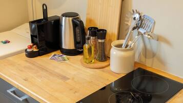 Una encimera de cocina con una cafetera, un hervidor, una botella de aceite, un especiero y un juego de utensilios.