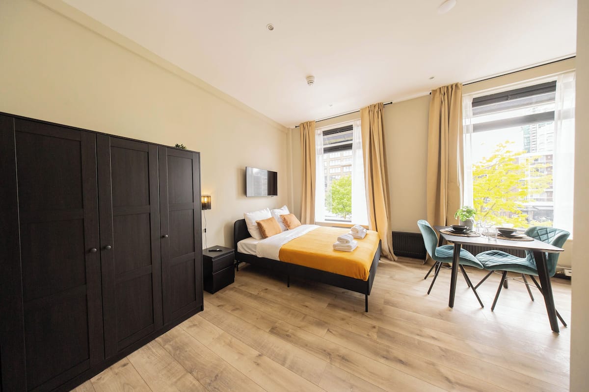 Un dormitorio moderno con cama, mesita de noche, televisor y un área de comedor con sillas.