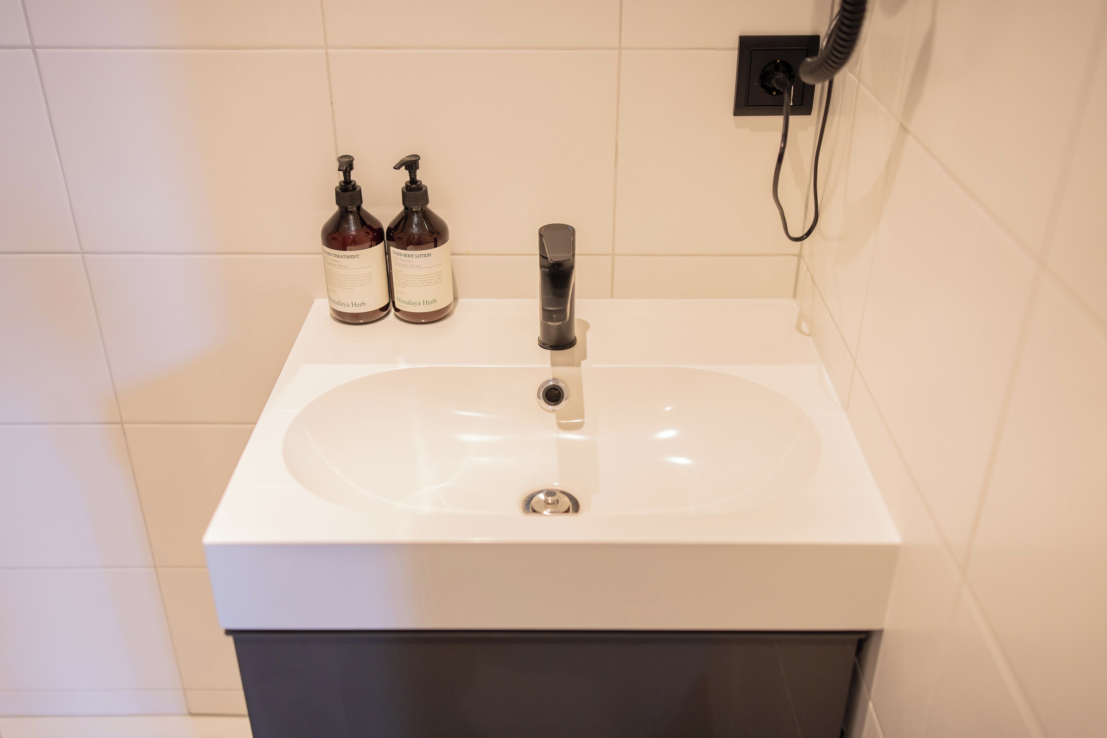 A bathroom with a white sink, two bottles of lotion, and a black faucet.