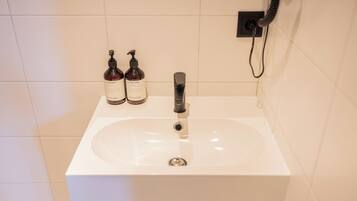 A bathroom with a white sink, two bottles of lotion, and a black faucet.