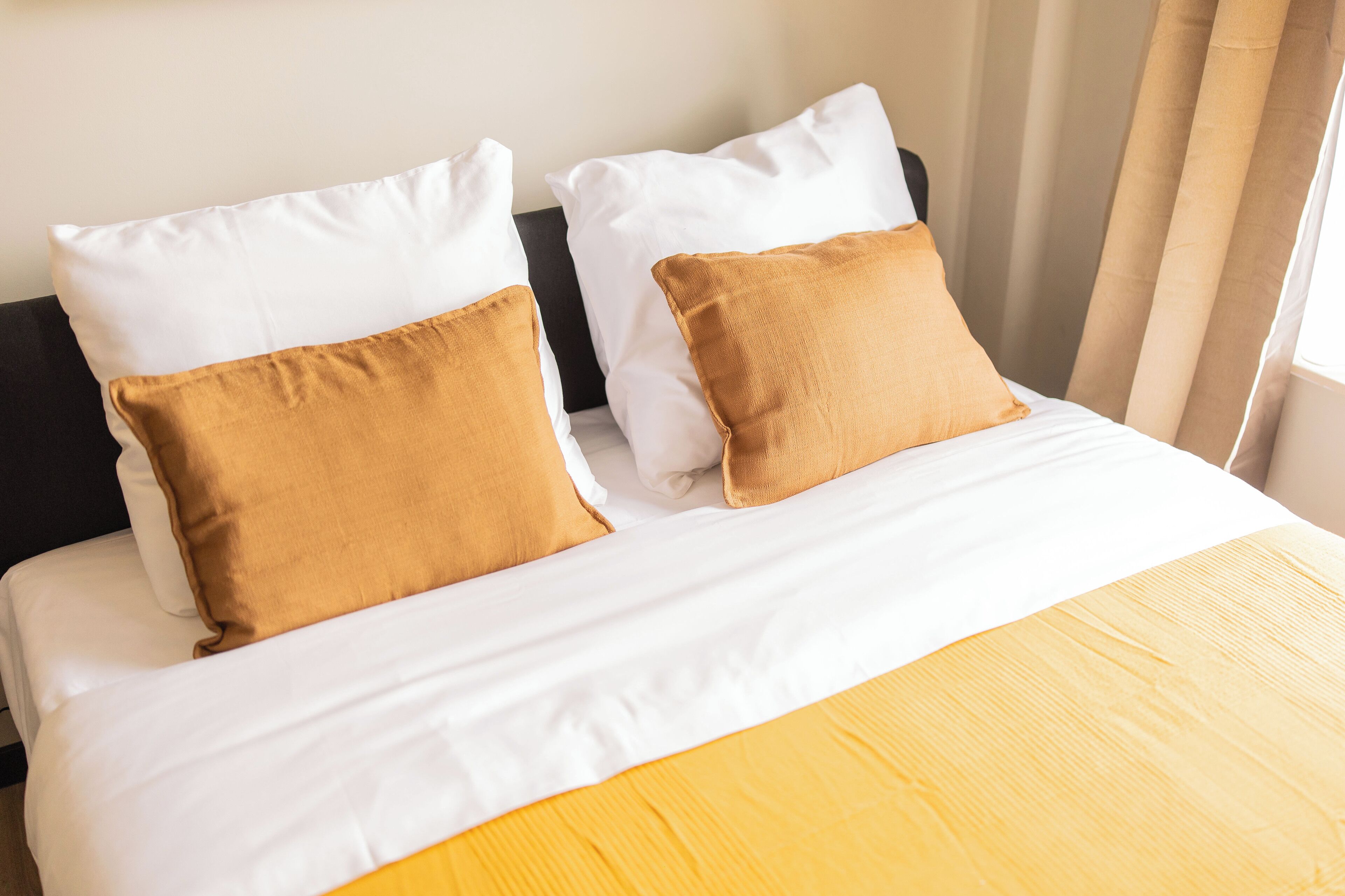 A bed with white and mustard pillows, a wooden headboard, and a yellow bedspread.
