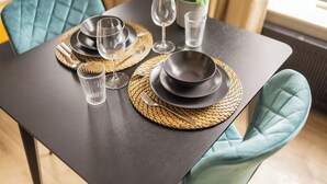 Une table à manger dressée avec des assiettes noires, des verres transparents et des sets de table en fibres tressées.