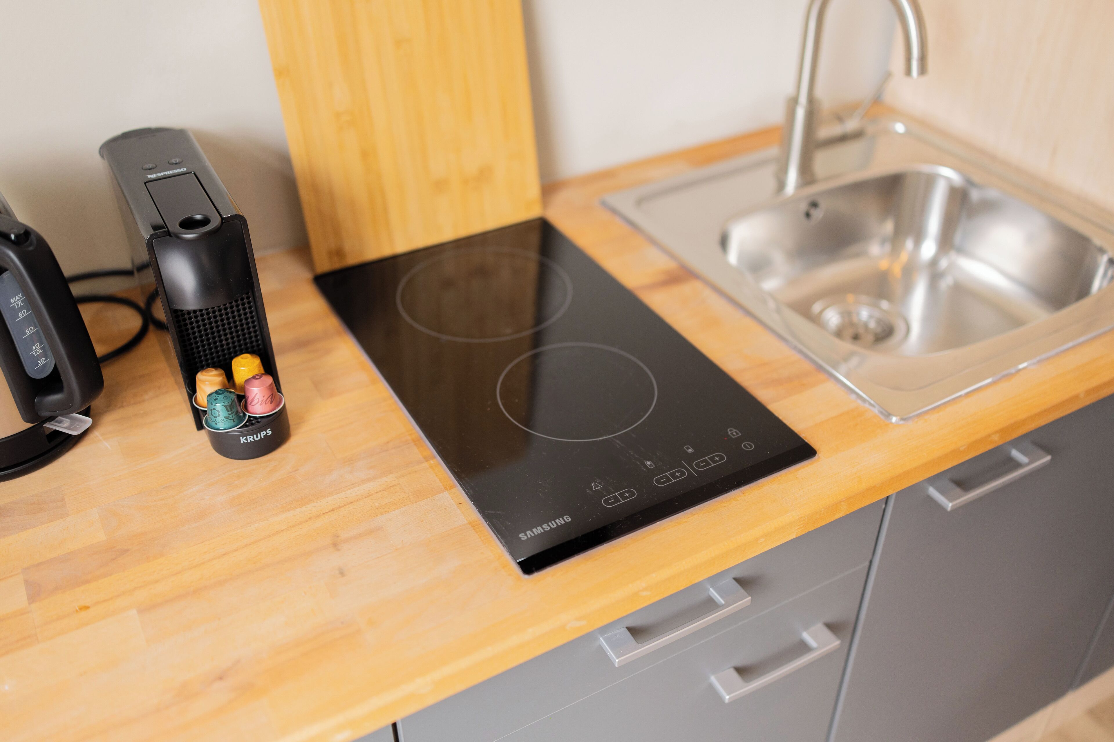 Een keuken met een geïntegreerd inductiekookveld, een roestvrijstalen spoelbak en een KRUPS elektrische waterkoker.