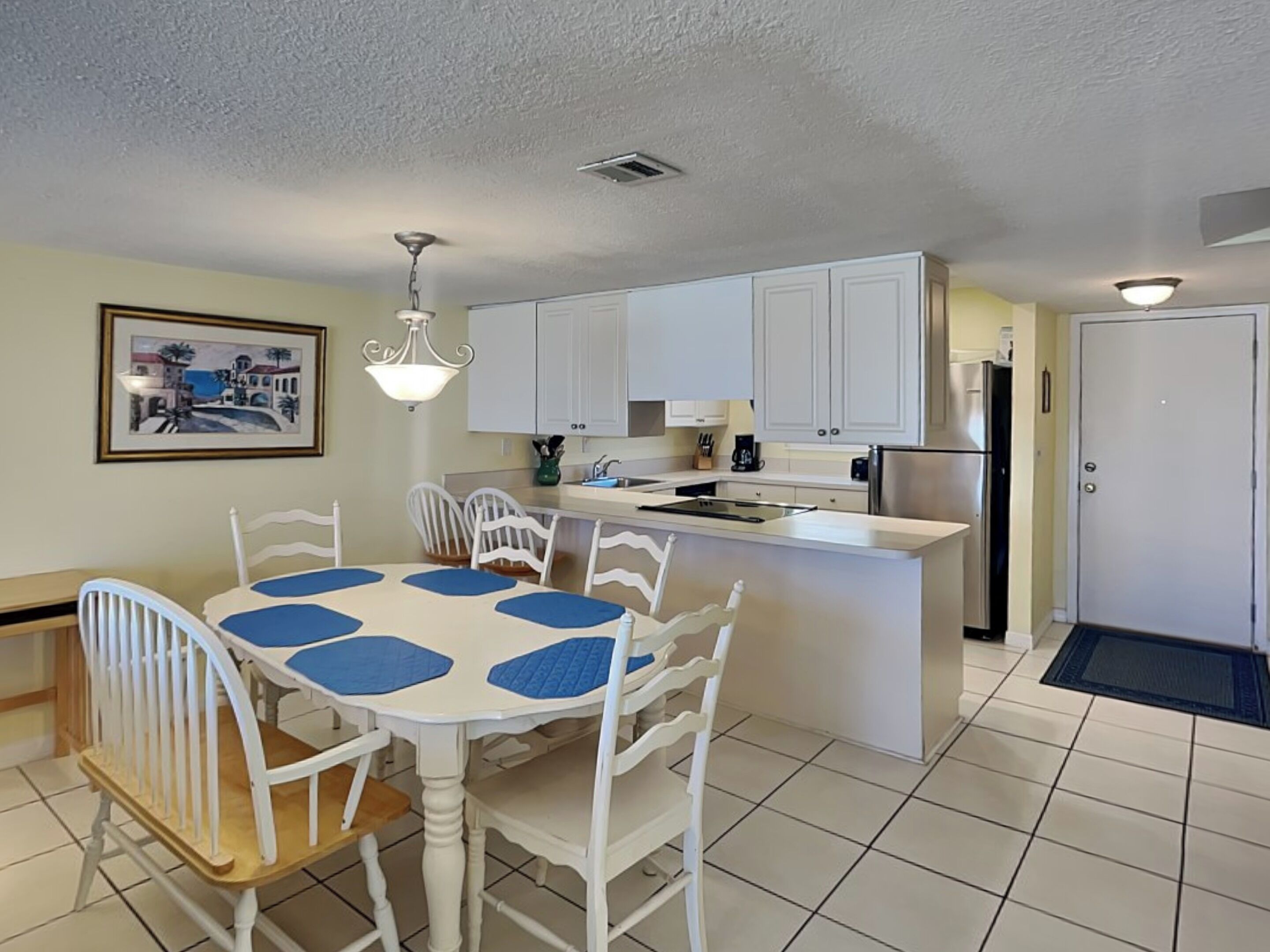 A compact kitchen with white cabinets, a central island, and a dining table with blue placemats.