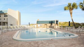 A swimming pool with lounge chairs and a building in the background. - Trade Winds 31 by Distinctive Beach Rentals (St. Augustine)