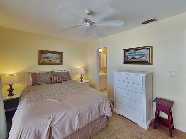 A bedroom with a bed, a nightstand, a dresser, a ceiling fan, and two framed pictures on the wall.