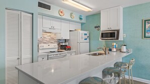 A modern kitchen with white cabinets, a stainless steel refrigerator, a microwave, and a large island with bar stools. - Blue Surf 2 (Miramar Beach)