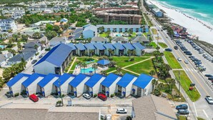 A coastal hotel with multiple blue-roofed buildings, a parking lot, and a beach view. - Blue Surf 2 (Miramar Beach)