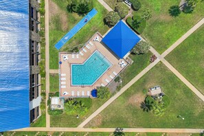 En vy från ovan av ett semesterområde med en swimmingpool, solstolar och en tennisbana.