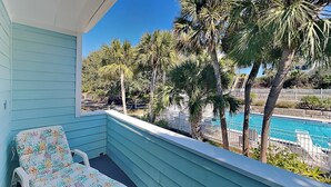 A balcony with a single lounge chair, overlooking a swimming pool surrounded by palm trees. - Quail Hollow B3-1TH by Distinctive Beach Rentals (St. Augustine)