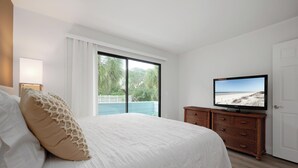 A bedroom with a bed, a television, a window with a view of the outdoors, and a door. - Quail Hollow B3-1TH by Distinctive Beach Rentals (St. Augustine)
