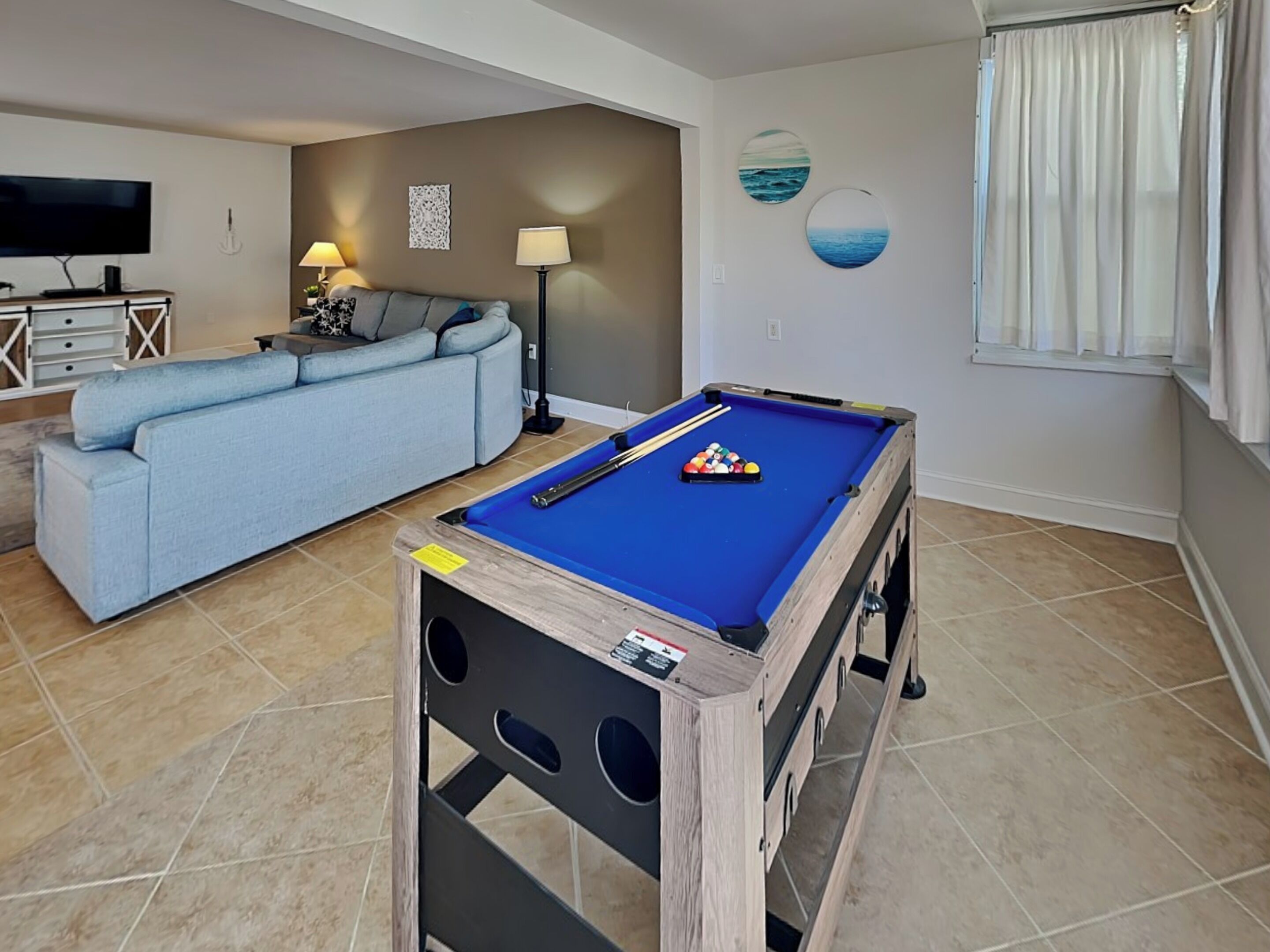 Una sala de estar con mesa de billar, un sofá, un televisor y una lámpara.