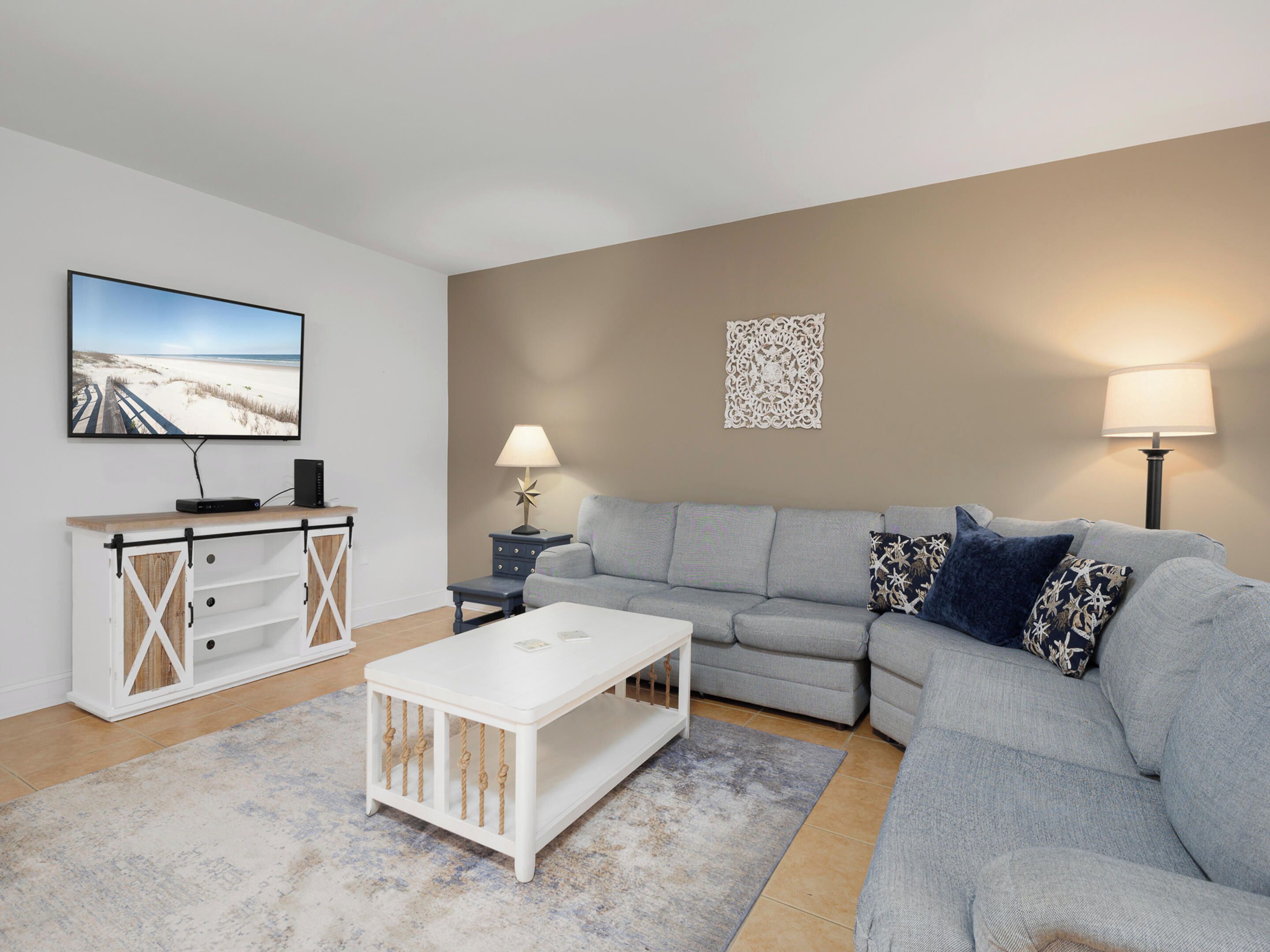 A living room with a grey sofa, a white coffee table, a TV on a wooden stand, and two lamps.