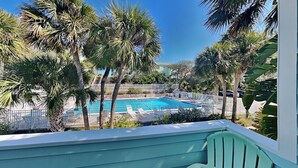 A pool area with a clear blue pool, surrounded by palm trees and a white fence. - Quail Hollow B3-1TH by Distinctive Beach Rentals (St. Augustine)