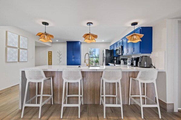 A modern kitchen with blue cabinets, a white island with bar stools, and pendant lights.