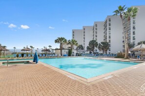 A swimming pool with lounge chairs, palm trees, and a multi-story building in the background. - Saida I Zen by the Sea (South Padre Island)