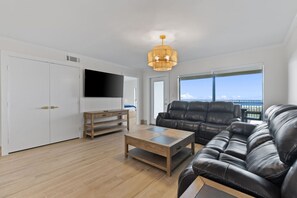 A spacious living room with a large leather sofa, a wooden coffee table, and a flat-screen TV mounted on the wall.