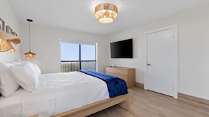 Un dormitorio moderno con cama, mesita de noche, televisor y ventana con vistas.